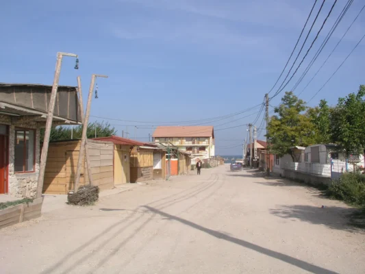 A dusty main street in Vama Veche, 2004, with wooden shacks and power lines leading down to the sea.