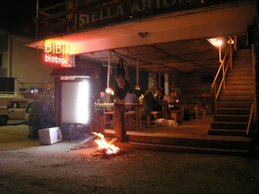 Night scene in Vama Veche, with people sitting at Bibi Bistro, a fire burning outside under neon lights.