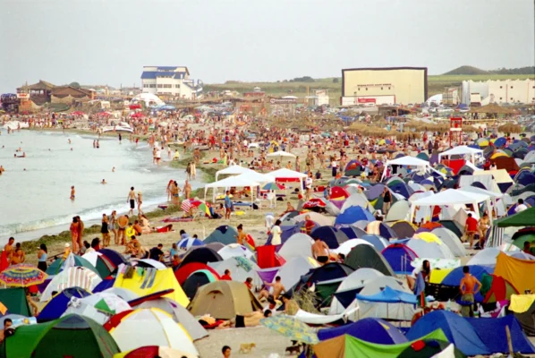 Crowded tents lining the beach in Vama Veche, 2003, waves crashing against a shoreline filled with campers.