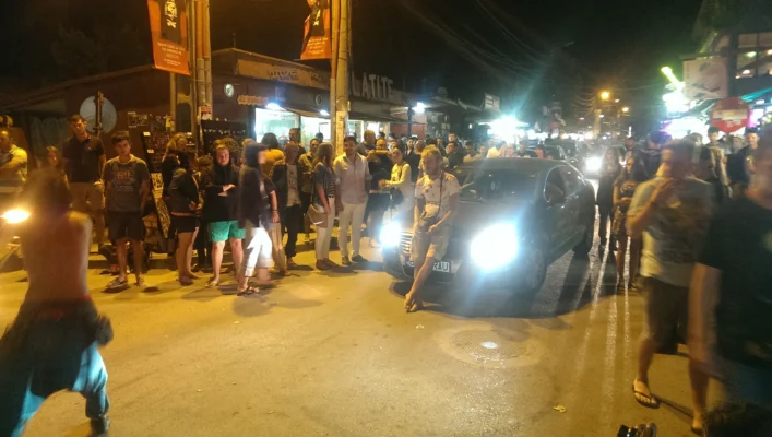 Man sitting on a car on a crowded street at night.