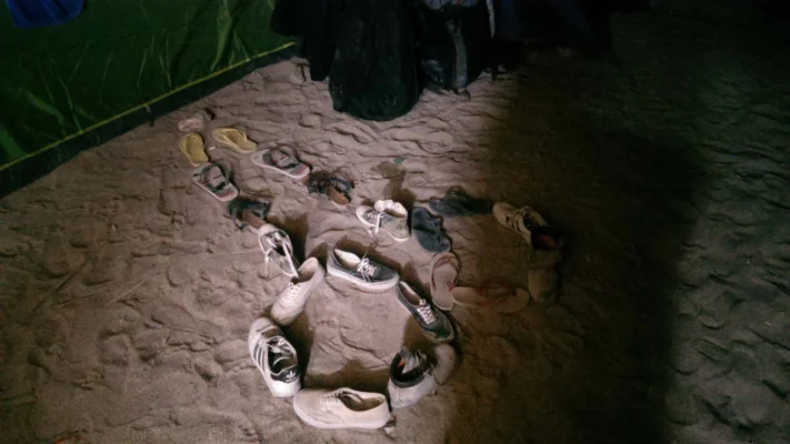 Shoes and sandals arranged in a phallus on the sand outside a tent.