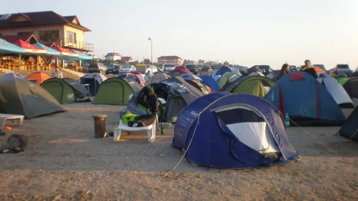 A cluster of colorful tents set up on the sand in 2 Mai, Romania, 2009, with people waking up in sleeping bags under the morning light.