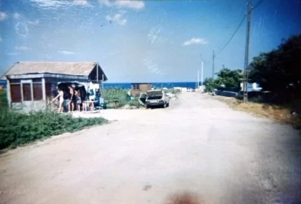 View down the main dirt road to the sea at Vama Veche in the 1980s, showing a small shack shop and a parked Dacia automobile.