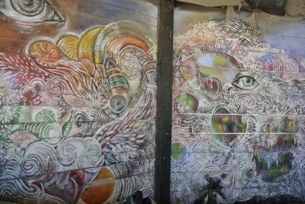 A colorful mural painted on wooden boards inside a Vama Veche bar, featuring eyes and swirling abstract patterns.