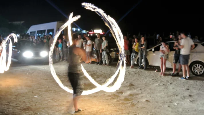 Large crowd gathered in Vama Veche’s main street at night, watching a fire dancer perform.