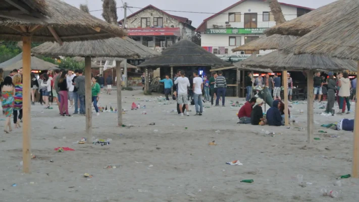 Beach after a night of partying, scattered with bottles, cans, and groups of people still awake.