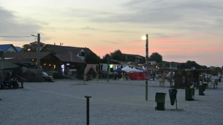 Sunset over Vama Veche, with beach bars and tents lit up in the distance.