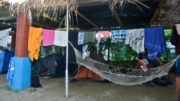 Hammock strung under a makeshift roof with colorful laundry drying on a line, tents pitched in the background.