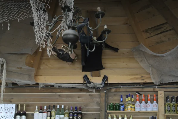 Inside a Vama Veche bar, bras, heels, and clothes hang from a chandelier above bottles of alcohol.