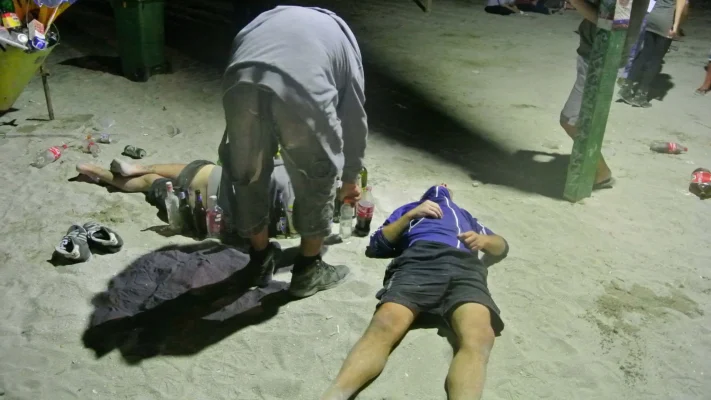 Two people lying on the sand at night, surrounded by empty bottles and soda.