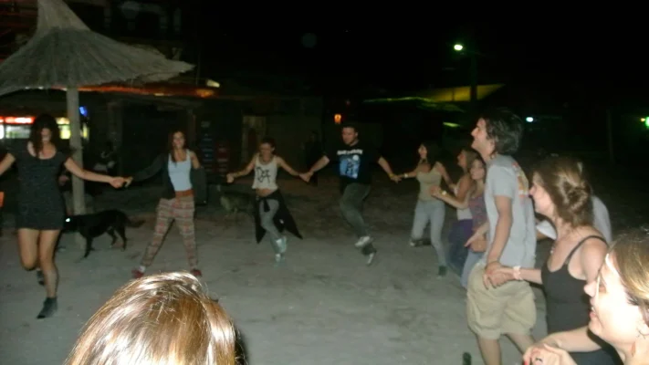 Group of young people holding hands and dancing in a circle on the sand at night.