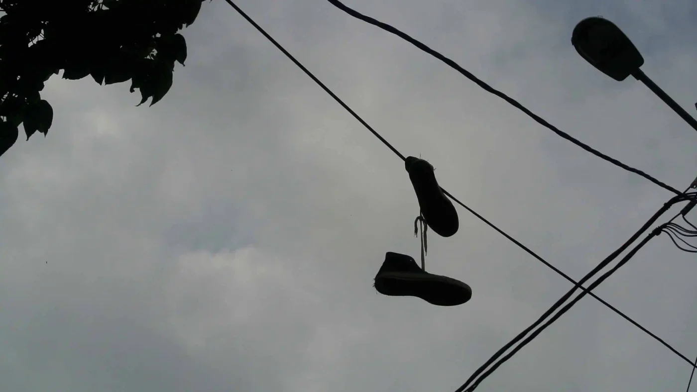 A pair of sneakers dangling from a power line against a cloudy sky.