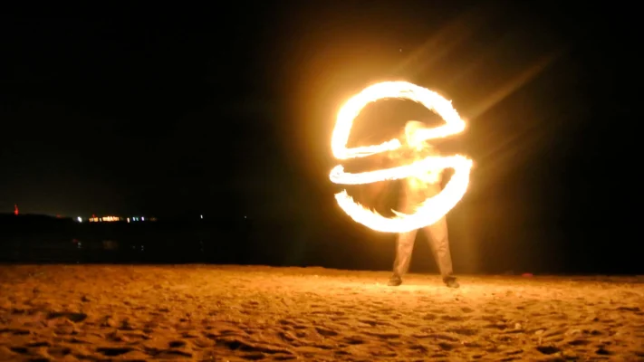 Long-exposure photo of a fire performer creating bright overlapping circles of flame on the beach.
