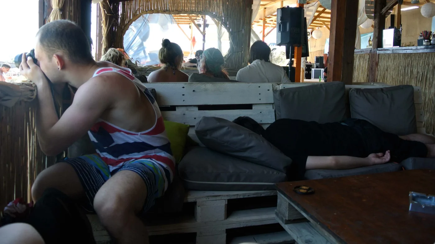 Inside a beach bar in Vama Veche - one friend snapping photos through the window, another collapsed on a couch, lost to the afternoon haze.