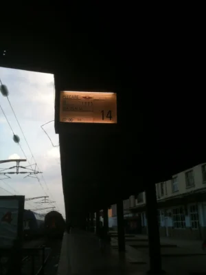 A dimly lit train platform in Bucharest, showing the departure board for train IR 1985 to Mangalia at 07:00, platform 14.