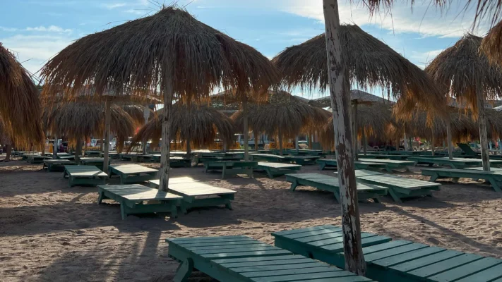ows of empty wooden loungers and straw parasols on the beach.