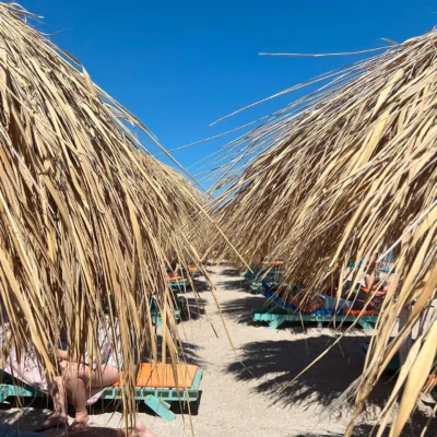 Rows of straw umbrellas with wooden loungers beneath, seen from between two close canopies.
