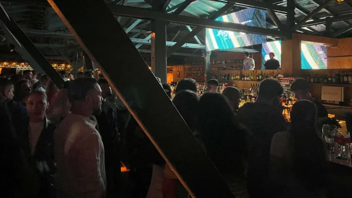 Packed modern bar interior with screens above the DJ booth.