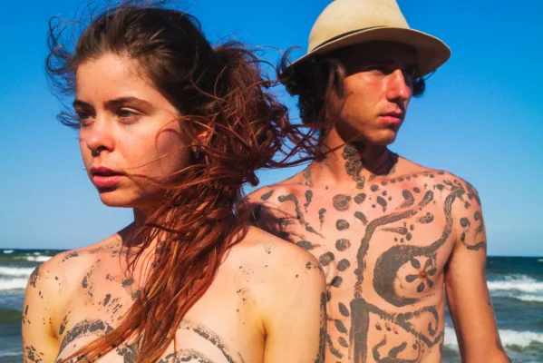 Two young people in Vama Veche, with tribal body paint and windswept hair, gazing toward the sea.
