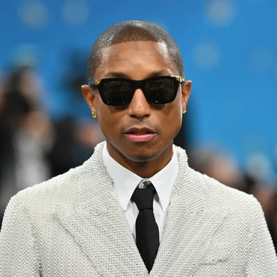 Pharrell Williams in a pearl-white textured suit with black tie and sunglasses.