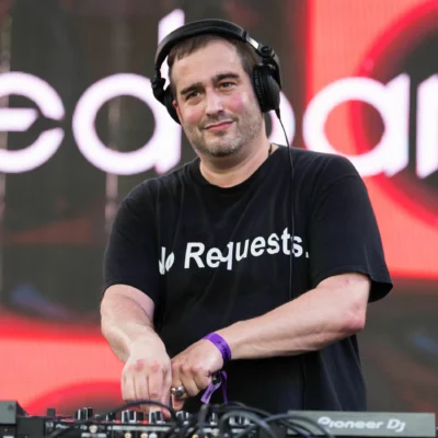 Todd Edwards performing on stage with headphones, wearing a black t-shirt that reads “No Requests.”