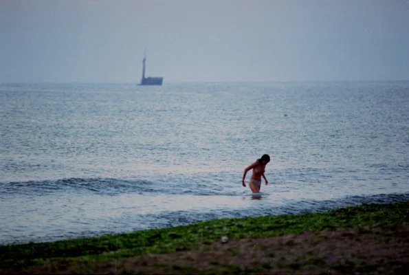 Swimmer in the shallow Black Sea at Vama Veche, with the Akra Aktion shipwreck fading in the background.