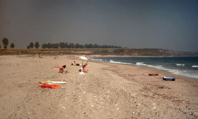 Sparse summer crowd on the wide, undeveloped beach at Vama Veche in the 1980s, with dunes and farmland visible in the distance.