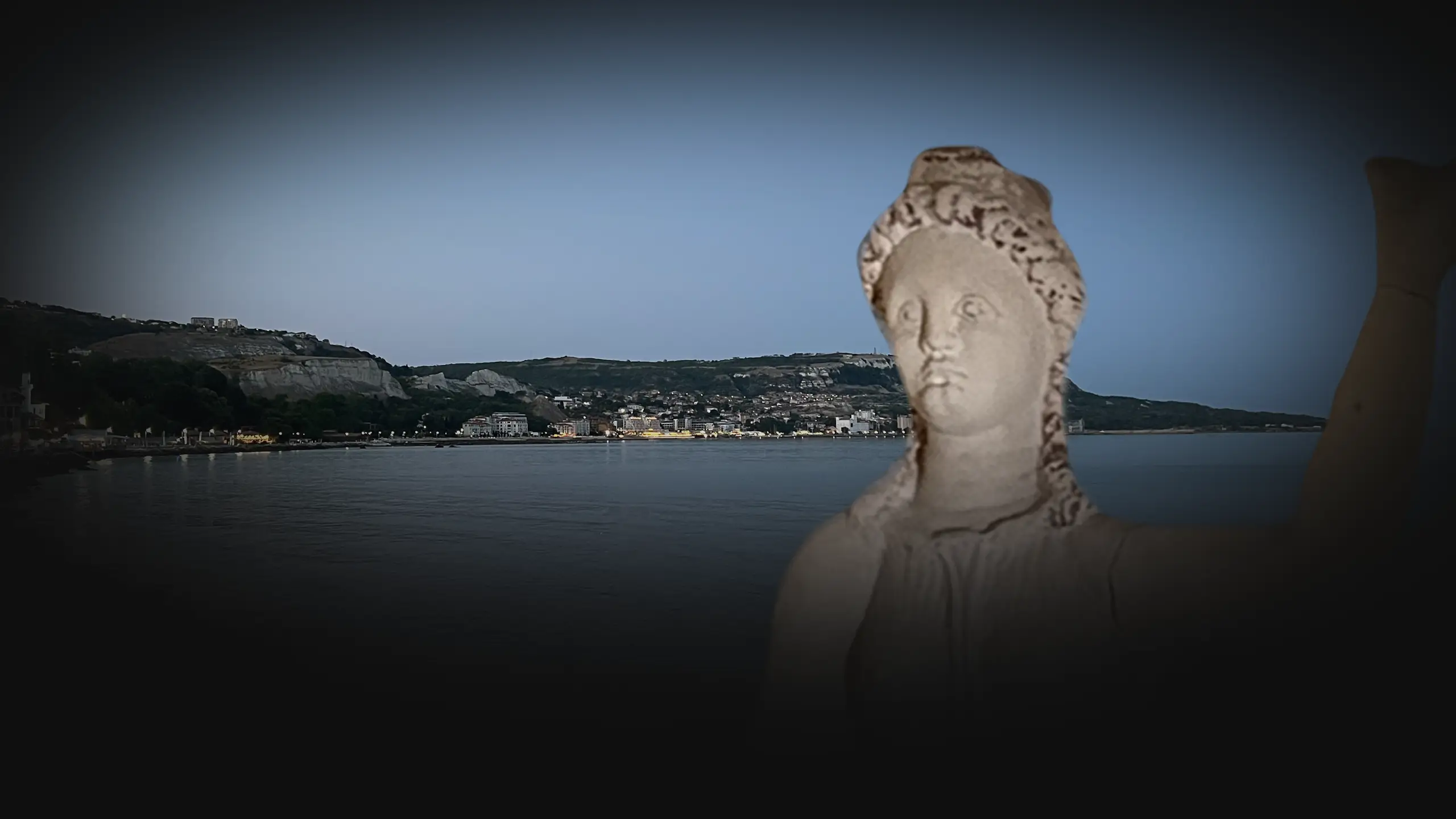 Blue-hour coast of Balchik on the Black Sea, with the half-bust of a Thracian statue subtly emerging from the cliffs like a memory of the past.