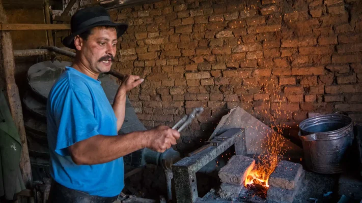 Blacksmith working beside a forge in Viscri, with sparks rising against an old brick wall.
