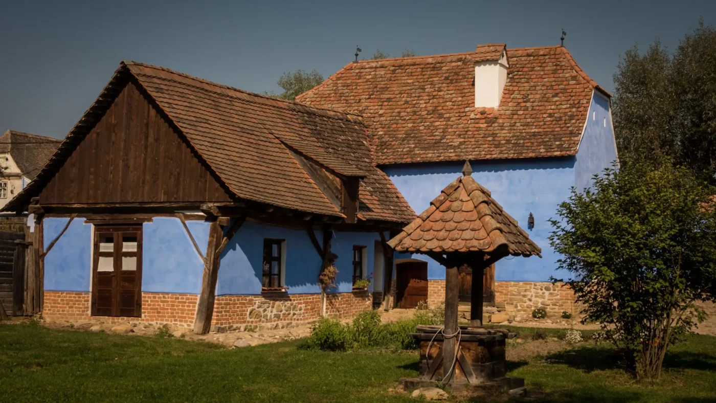 Traditional blue-painted Saxon house in Viscri associated with King Charles III, with timber outbuildings and a tiled well in the courtyard.