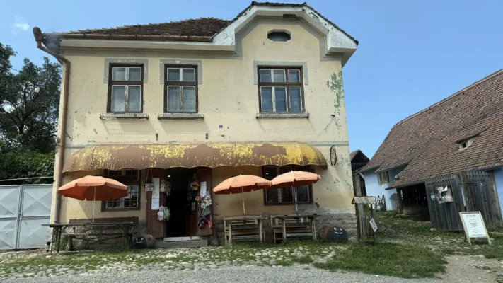 Traditional village shop in Viscri with orange umbrellas, souvenir displays and weathered plaster facade.