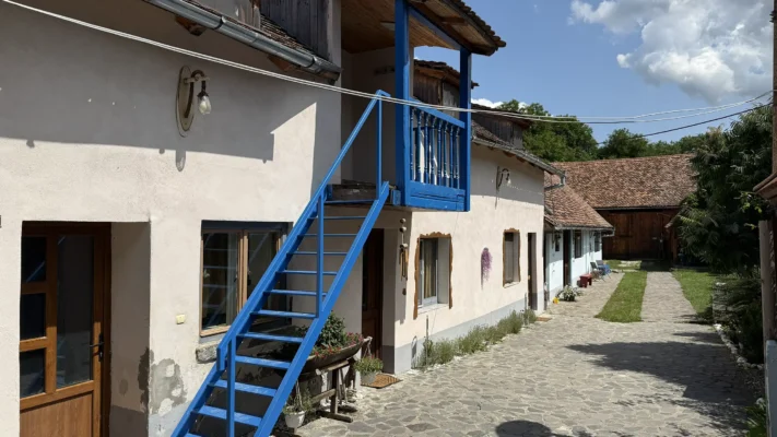 Traditional courtyard in Viscri with whitewashed buildings, a bright blue wooden staircase and cobbled paving.