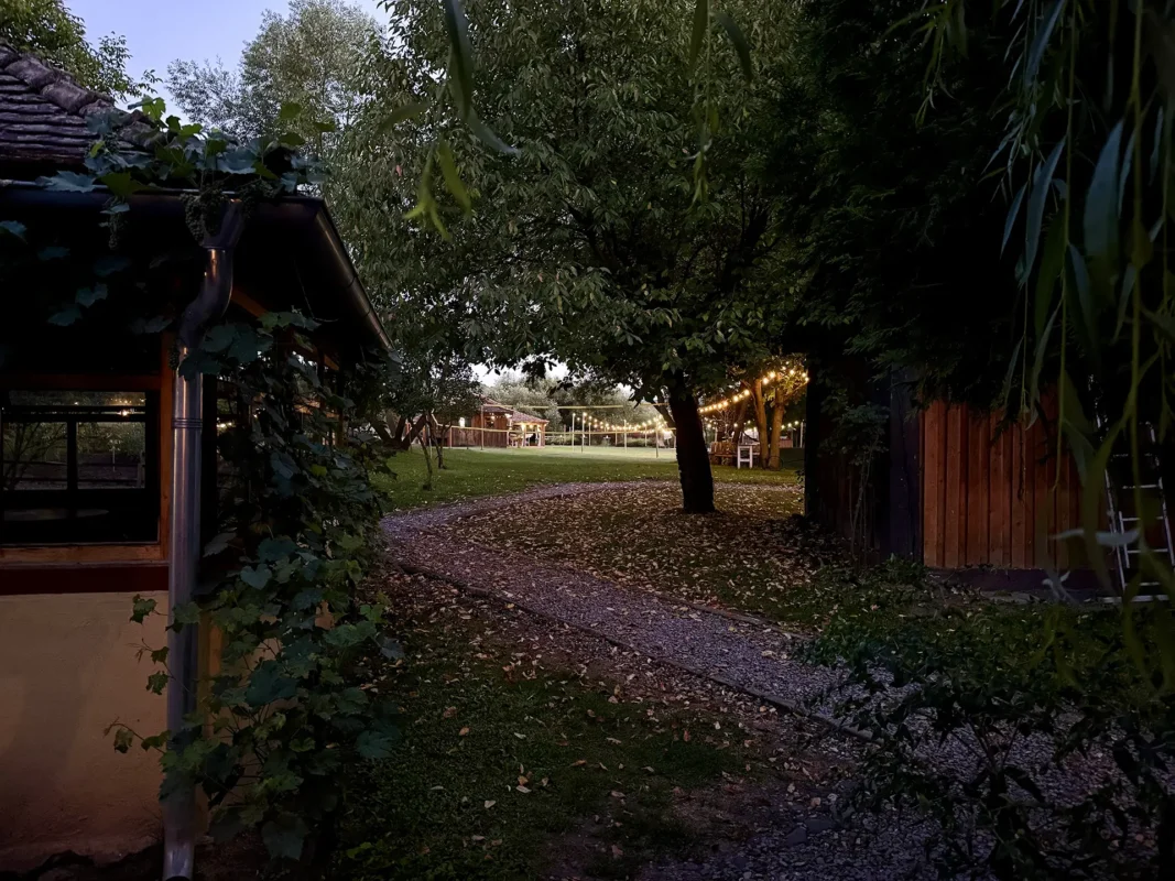Valea Verde garden in Cund at dusk, with warm string lights glowing between trees and wooden buildings.