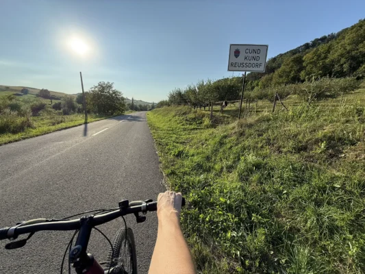 Cyclist approaching the Cund, Kund, Reussdorf village sign on a quiet rural road at sunset.