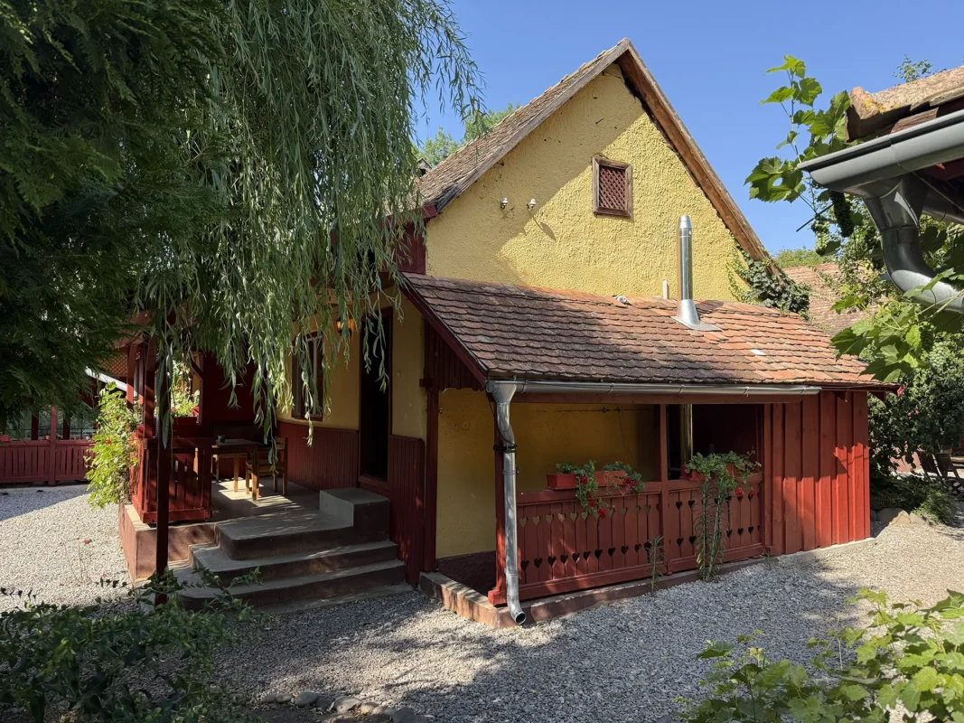 Small traditional guesthouse at Valea Verde Retreat in Cund, with yellow plaster walls, red timber details and a tiled roof.