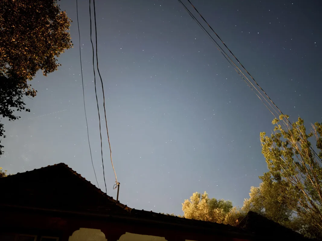 Star-filled night sky above the rooftops and utility lines of Cund, Transylvania.