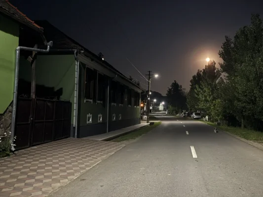 Quiet main street of Cund at night, lined with traditional houses and streetlights beneath a bright moon.