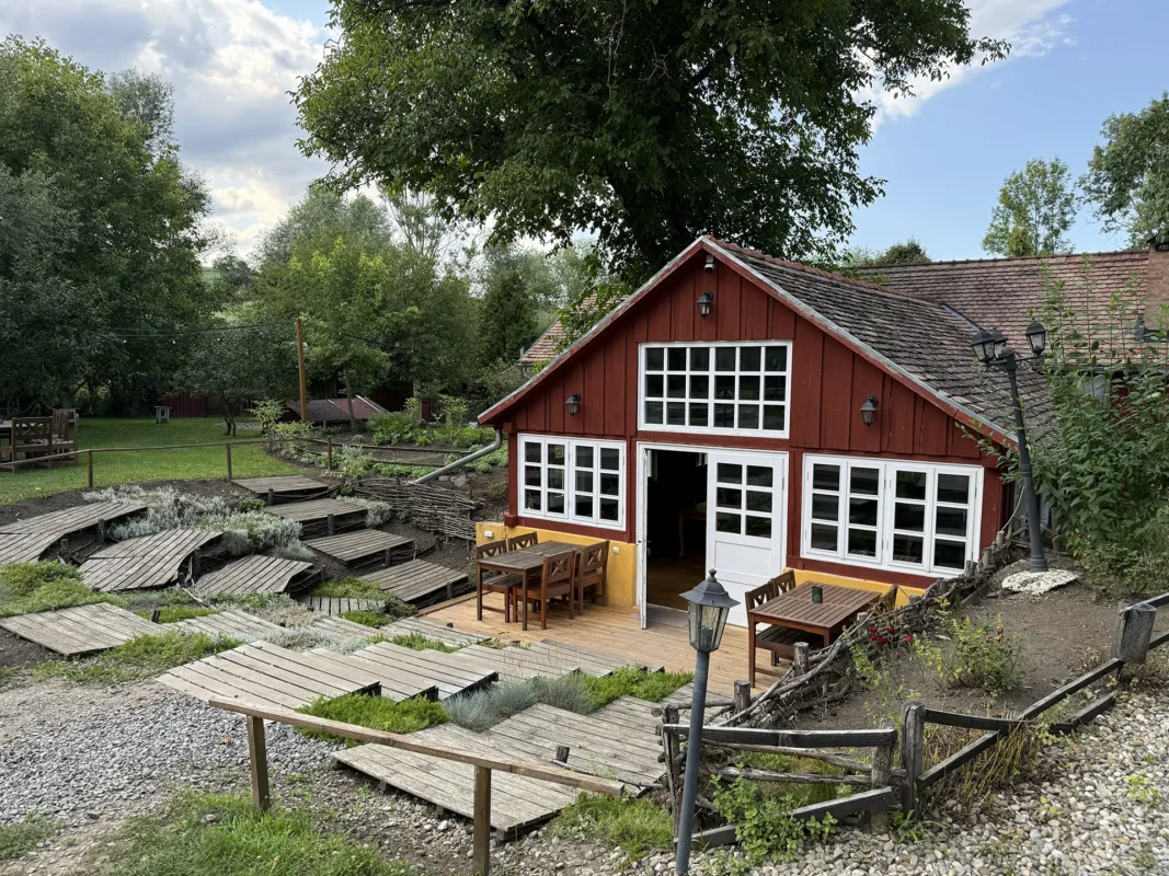 Valea Verde restaurant in Cund, a red timber building with white windows surrounded by terraced garden paths and greenery.