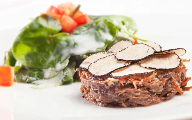 Fine-dining meat dish topped with sliced black truffle and served with a green salad at Valea Verde restaurant.