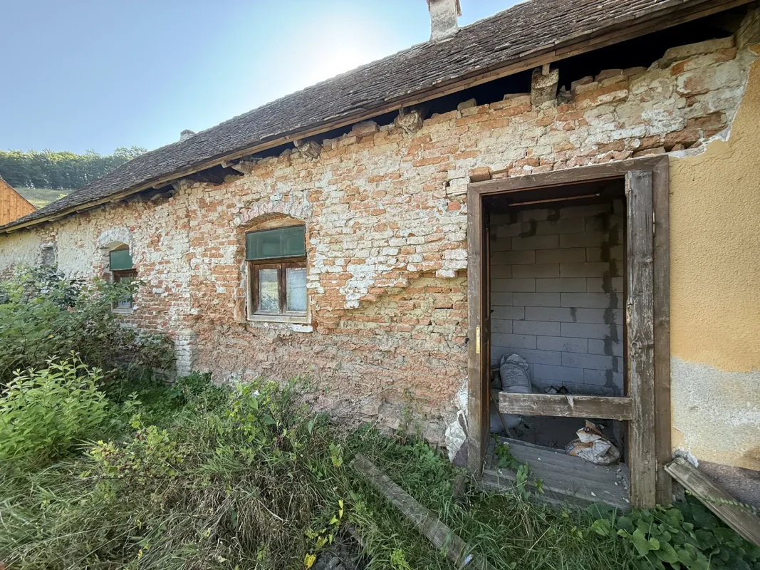Old Saxon house in Cund, Transylvania, with a tiled roof, wooden gate and partially collapsed brick wall.